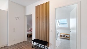 Un interior moderno con un banco de madera, un reloj y vistas a un área de lavandería por una puerta abierta.