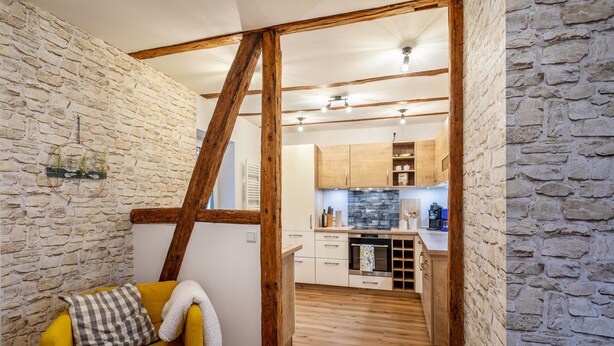 A room with a yellow sofa, a wooden ladder, and a kitchen in the background.