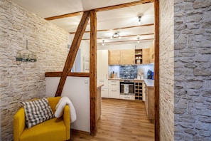 Une pièce avec un canapé jaune, une échelle en bois et une cuisine à l’arrière-plan.