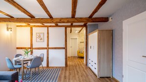 A room with a wooden ceiling, a dining area with a table and chairs, a sofa, a cabinet, and a door.