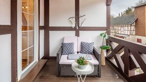 A balcony with a wicker sofa, a small table with a plant, and a decorative hanging piece.