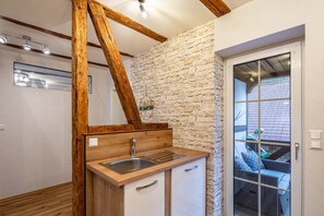 Une cuisine avec un mur en pierre, des poutres en bois, un évier et une vue sur l’extérieur, visible à travers une porte vitrée.