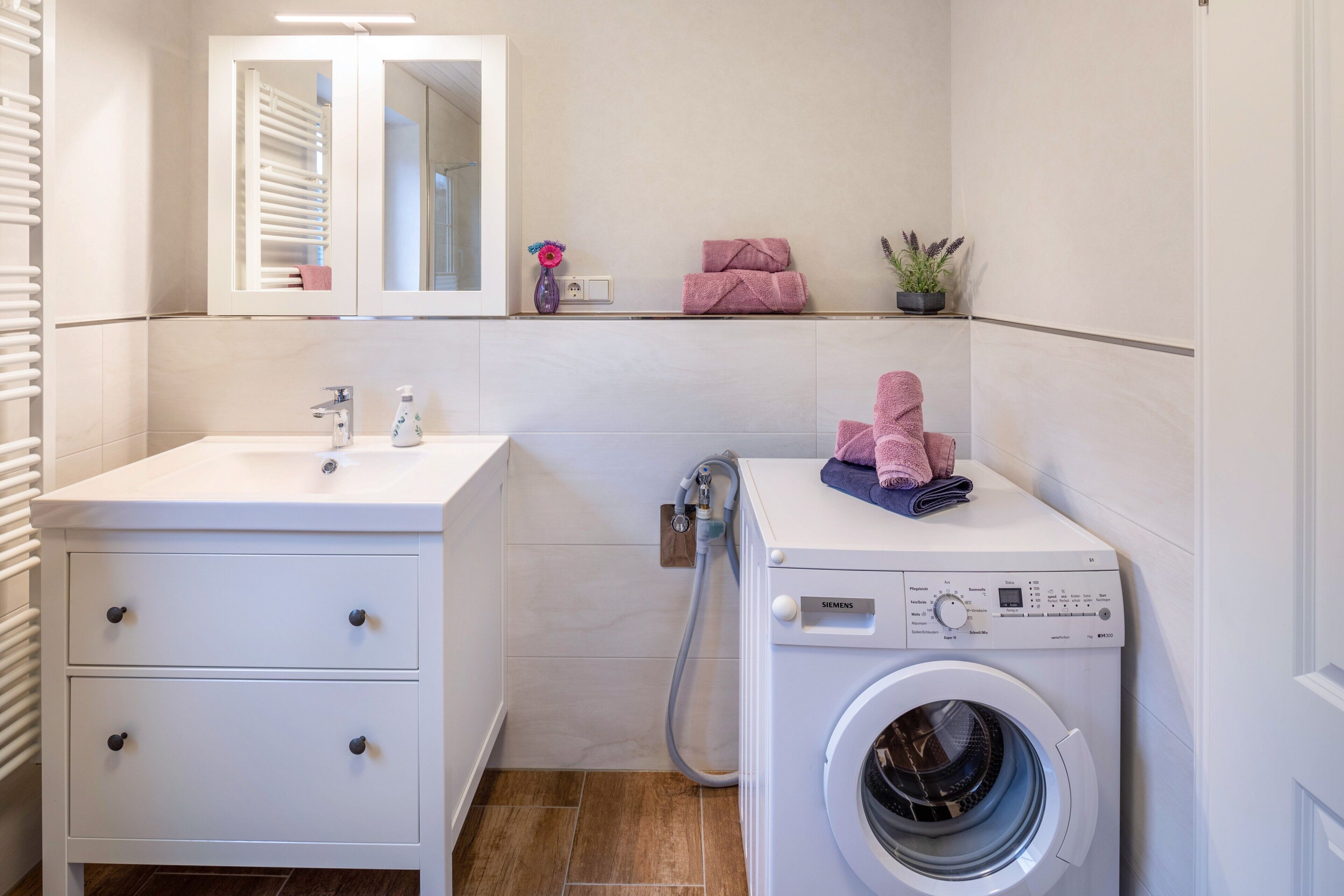 Une salle de bain moderne avec un lavabo blanc, un miroir, un lave-linge et un porte-serviettes.