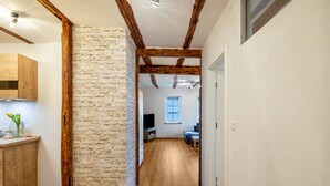 A hallway with exposed wooden beams, a stone wall, and a wooden floor leading to a room with a television and a window.