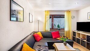 A modern living room with a sofa, a table, a TV, and a window with curtains. - Apartment "Waldeckchen" with Private Terrace & Wi-Fi (Waldeck)