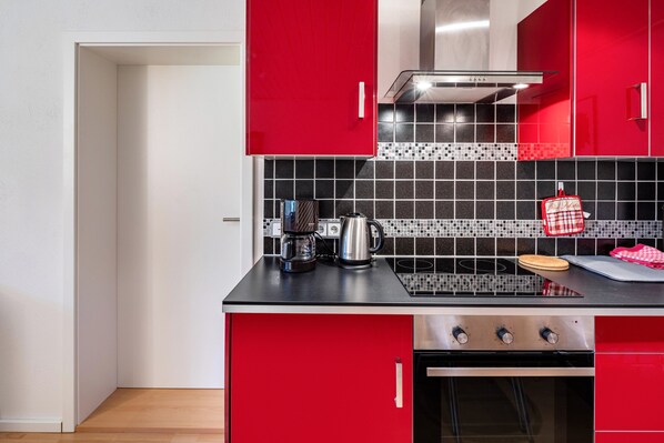 A kitchen with red cabinets, a black countertop, a stove, and a tiled backsplash. - Apartment "Waldeckchen" with Private Terrace & Wi-Fi (Waldeck)