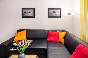 A black leather sofa with red and yellow cushions, a vase with yellow flowers, and two framed pictures on the wall. - Apartment "Waldeckchen" with Private Terrace & Wi-Fi (Waldeck)