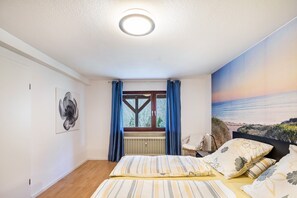 A bedroom with a bed, a radiator, a window with curtains, a chair, and a wall with a beach mural. - Apartment "Waldeckchen" with Private Terrace & Wi-Fi (Waldeck)