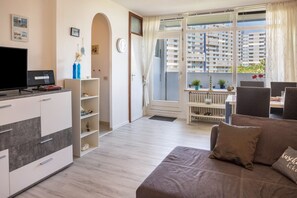 Ein modernes Wohnzimmer mit Flachbildfernseher, Sofa, Essbereich und Blick auf hohe Gebäude.