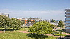 En byggnad med modern design, ett grönområde med träd och en klar himmel.