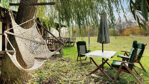 Eine Hängematte, ein Tisch und zwei Stühle in einer grünen Außenanlage.