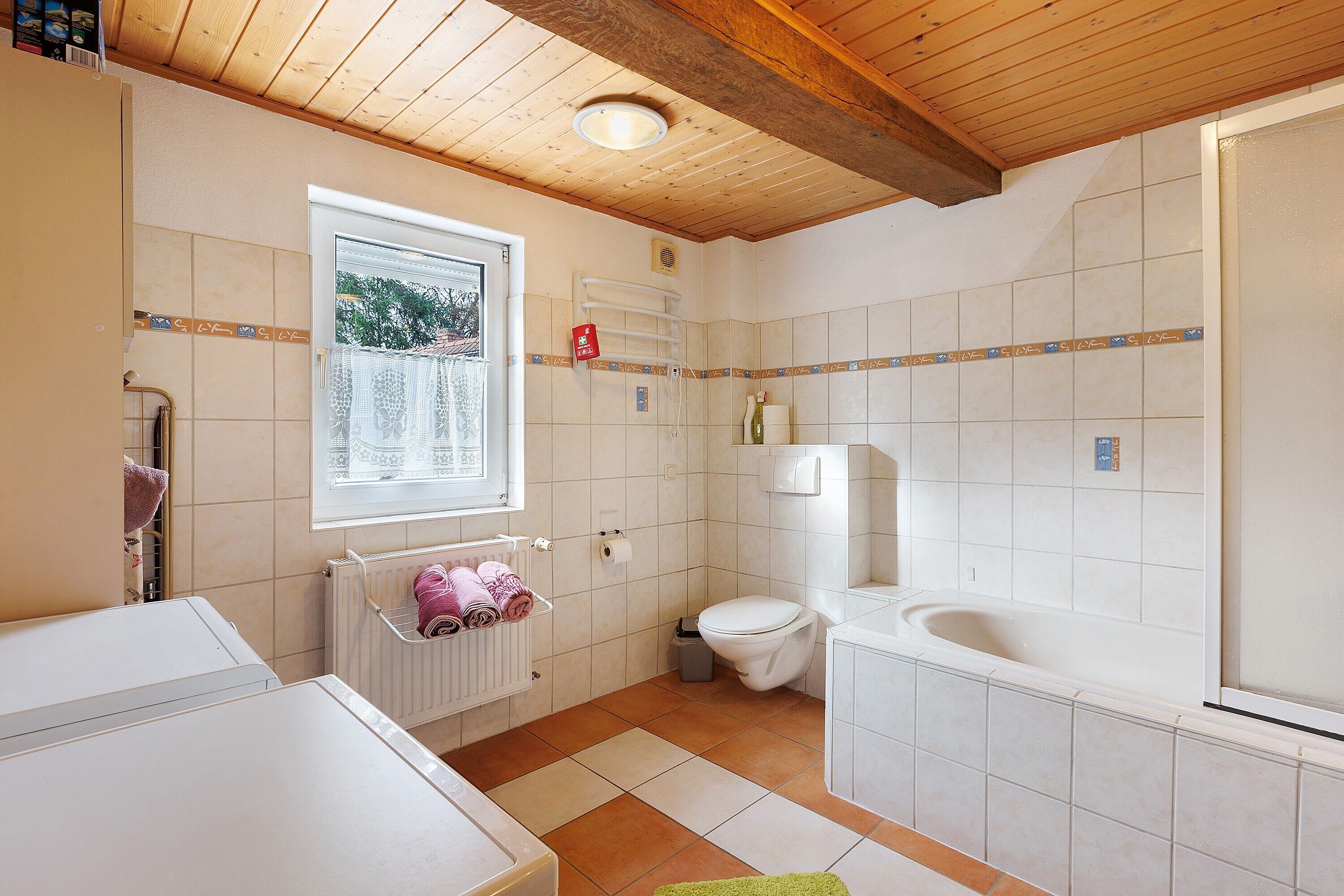 A bathroom with a window, a radiator, a toilet, and a bathtub.