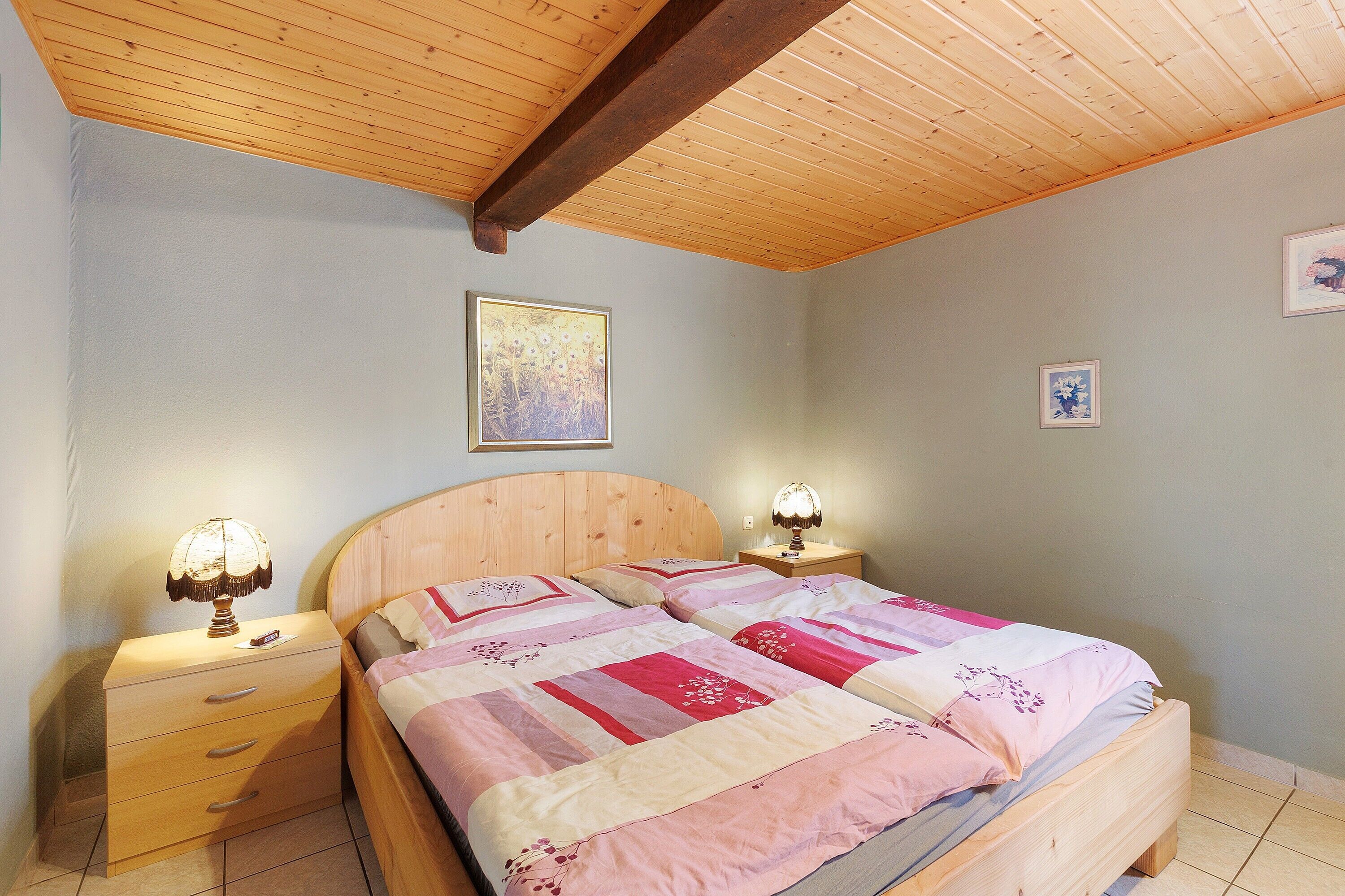Camera da letto con una testiera in legno, due comodini con lampade, un letto con copriletto e un quadro appeso alla parete.