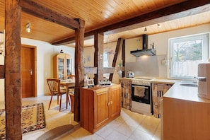 A kitchen with wooden cabinets, a dining area with a chair, and a window.