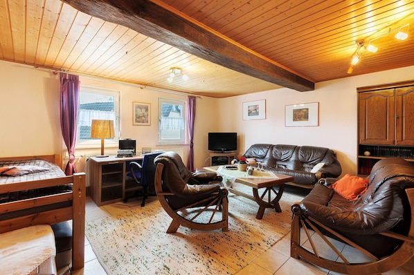 A cozy room with a wooden ceiling, a bed, a desk with a computer, a leather sofa, and a television.