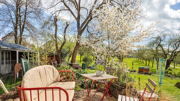 Un jardín con un banco de metal rojo, una mesa de madera y un sofá blanco.