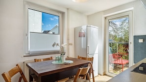Un comedor con una mesa de madera, sillas, un refrigerador y una ventana con persianas.