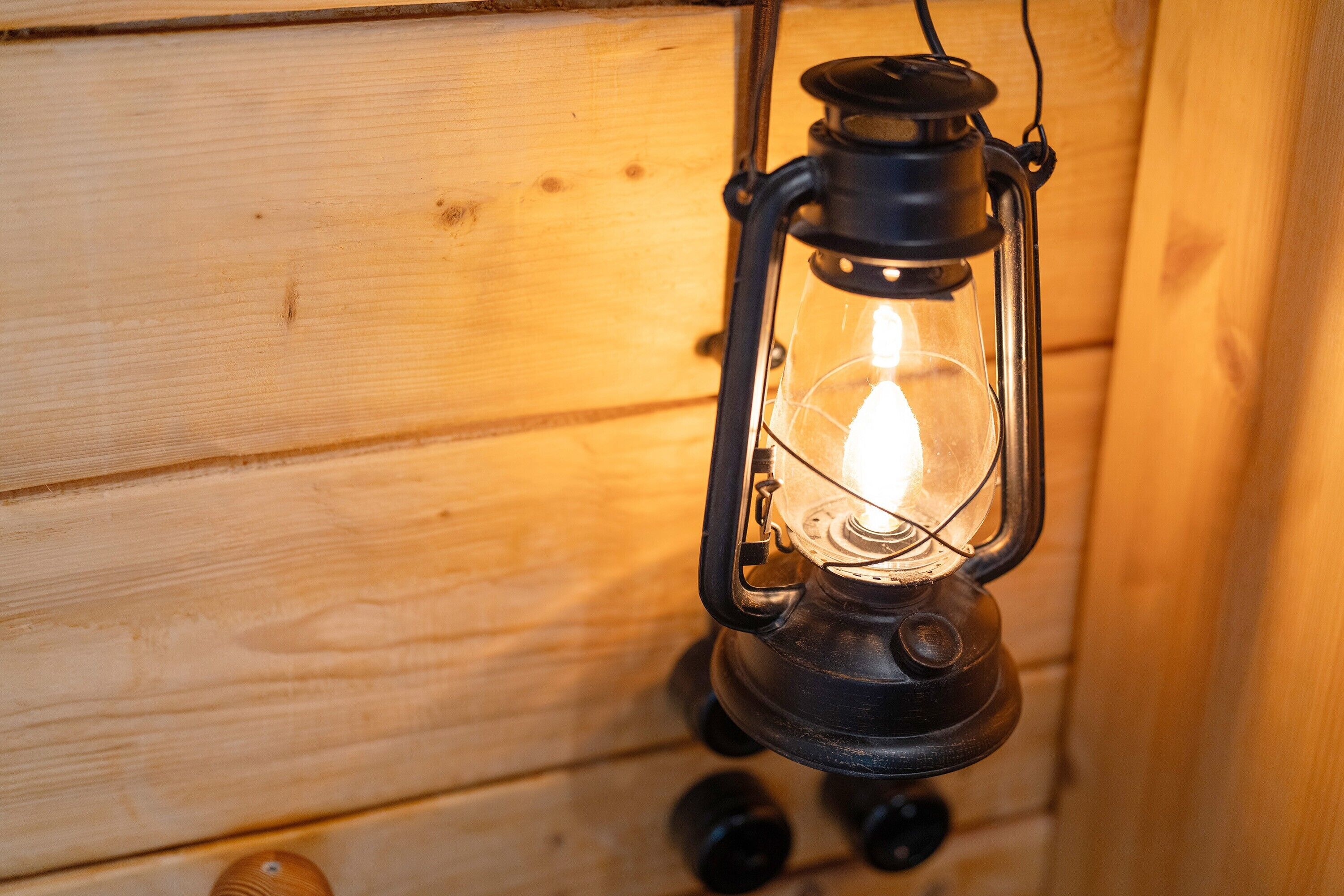 Een lantaarn met zichtbare gloeilamp, hangend aan een houten wand.