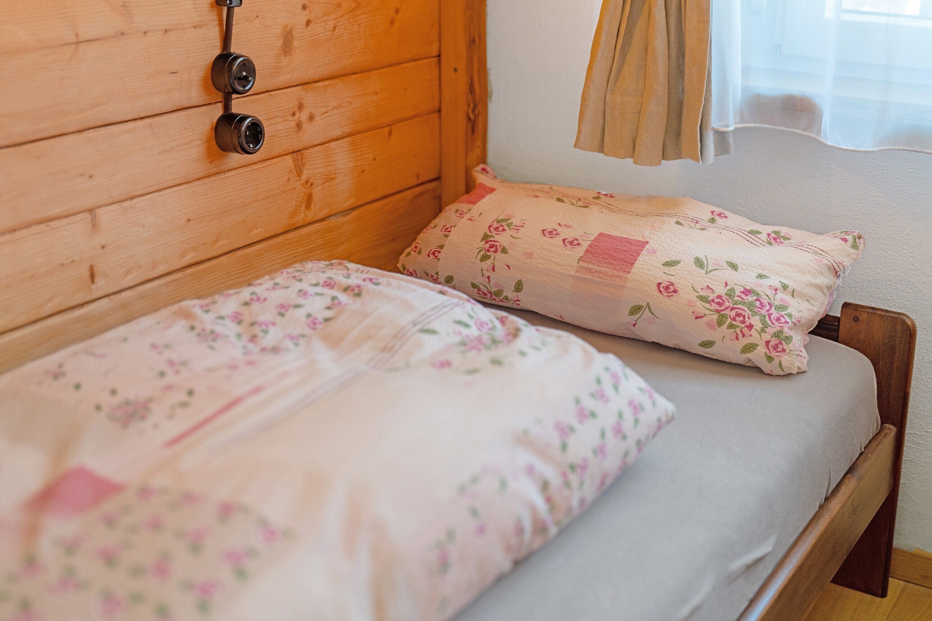 A wooden bed with floral bedding and a headboard with a light fixture.