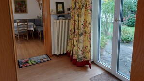 Ett rum med en matplats, ett element, en gardin och utsikt över trädgården genom en glasdörr.