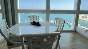 A dining area with a round table and four chairs, overlooking a marina with boats and a pier.