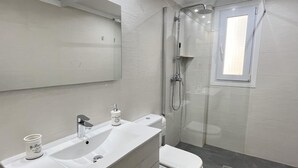 Ein modernes Badezimmer mit einem weißen Waschtisch, einer Toilette, einer Duschkabine aus Glas und einem großen Spiegel.