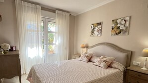 Ein Schlafzimmer mit einem großen Bett, zwei Nachttischen, einer Kommode und einem Fenster mit Vorhängen.