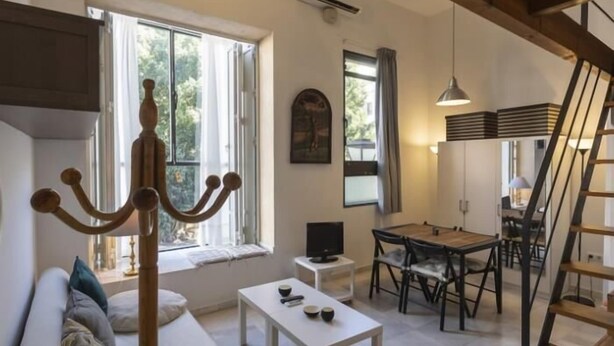A modern living room with a sofa, a coffee table, a dining area with a table and chairs, a staircase, and a large window providing natural light. - Dreams of the Sevilla Oasis in old town (Sevilla)