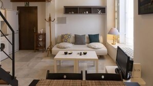 A modern living room with a sofa, a coffee table, and a TV. There is a staircase leading to an upper level, and a window with a painting. - Dreams of the Sevilla Oasis in old town (Sevilla)