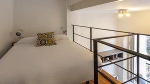 A bedroom with a bed, a patterned pillow, a nightstand, a window, and a balcony railing. - Dreams of the Sevilla Oasis in old town (Sevilla)