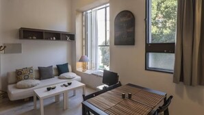 A modern living room with a sofa, coffee table, and dining table. There is a window with curtains, a lamp, and a shelf with decorative items. - Dreams of the Sevilla Oasis in old town (Sevilla)
