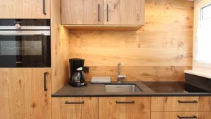 A modern kitchen with wooden cabinets, a black coffee maker, and a stainless steel sink. - Am Birkenhain by Interhome (Seefeld in Tirol)