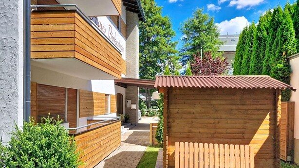 A modern building with a wooden facade, a visible sign reading 'Haus Birkenhain,' and a small wooden structure in the foreground. - Am Birkenhain by Interhome (Seefeld in Tirol)
