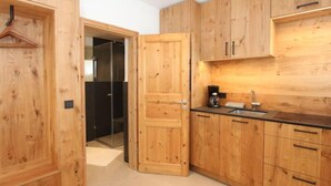 A modern kitchen with wooden cabinetry, a glass door leading to a bathroom, and a coffee maker on the countertop. - Am Birkenhain by Interhome (Seefeld in Tirol)