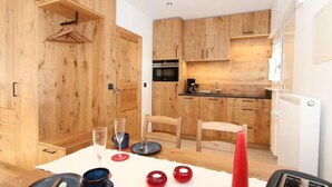A modern kitchen with wooden cabinets, a dining table with plates, cups, and glasses, and a toaster. - Am Birkenhain by Interhome (Seefeld in Tirol)
