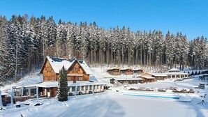 Un chalet enneigé, doté de plusieurs cabanes en bois, d’une piscine et entouré d’une forêt.