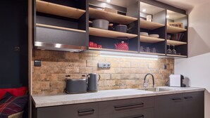 Une cuisine moderne avec un dosseret en pierre, des étagères en bois et des appareils électroménagers intégrés.