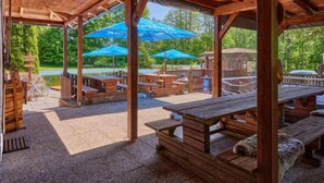 Un pavillon en bois installé à l’extérieur, doté de tables de pique-nique et de parasols bleus, et entouré de verdure.