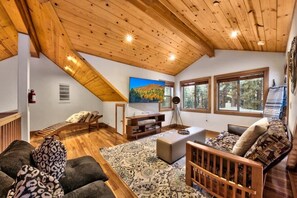 Ein gemütliches Interieur mit schrägverdeckter Decke, Holzmöbeln, einem großen Fenster und einem Gemälde an der Wand.