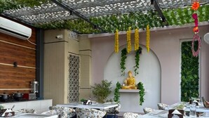 Un espace extérieur aménagé pour les repas, avec des tables et des chaises, une statue de Bouddha et de la verdure.