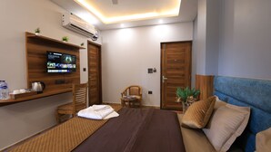 Une chambre d’hôtel moderne avec un lit, un téléviseur fixé au mur, une étagère en bois avec des articles de toilette, une chaise et un canapé bleu.