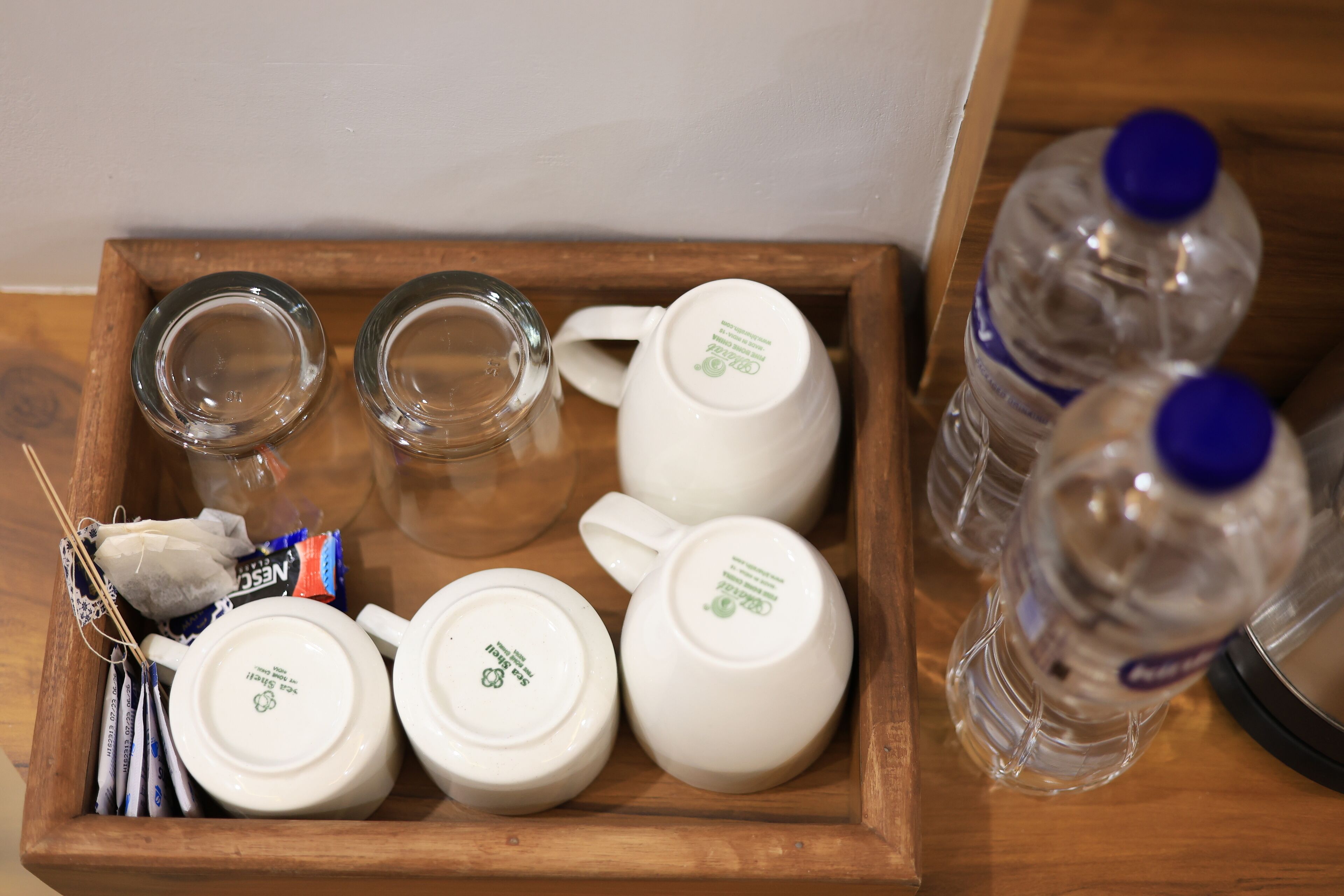 A wooden tray with a tea set, including a teapot, cups, and a glass, along with two water bottles.