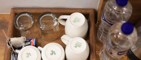 A wooden tray with a tea set, including a teapot, cups, and a glass, along with two water bottles.