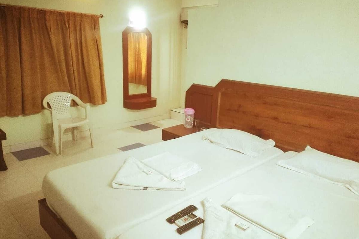 A hotel room with two beds, a chair, a mirror, and a nightstand.