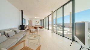 Ein modernes Wohnzimmer mit Sofa, Couchtisch und Sesseln, großen Fenstern mit Aussicht und einem Kamin.