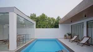 A modern outdoor swimming pool with glass walls, a wooden deck, and lounge chairs. - Rocks and Greens (Padmanabham)
