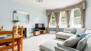 Ein Wohnzimmer mit Sofa, Fernseher und Esstisch.