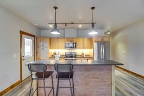 Une cuisine moderne avec des meubles en bois, des appareils en acier inoxydable et deux tabourets de bar.