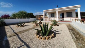 Un bâtiment blanc doté d’un balcon, entouré d’une cour en gravier où poussent de grands plants d’agave.