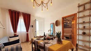 Un coin repas avec une table dressée pour quatre personnes, un lustre et une étagère en bois ornée de poteries.